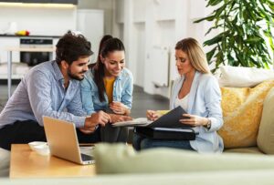 A couple reviews insurance documents beside a laptop, home inventory list, and vehicle records.